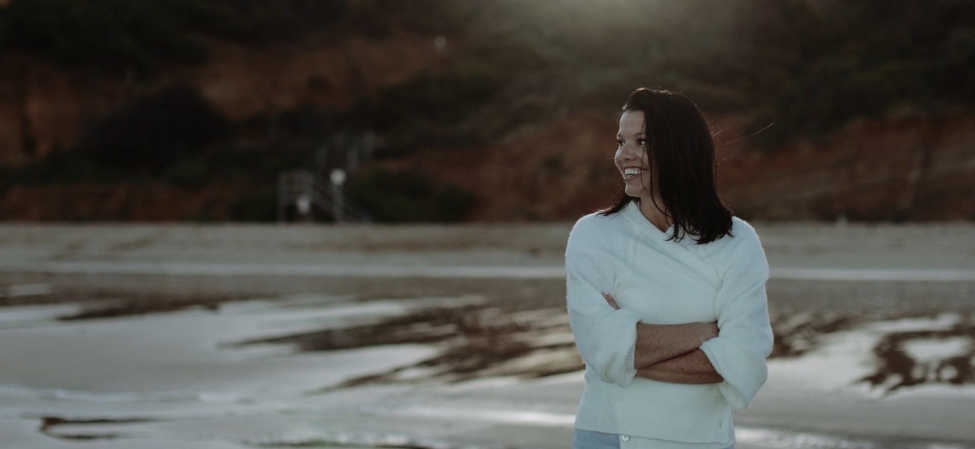 Jo Bets, creator of 'Grief - A Guided Journal' rugged up and smiling on a beach