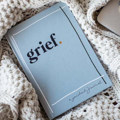The lovely blue book: 'Grief - A Guided Journal' created by Jo Betz sitting cozily in a knitted blanket